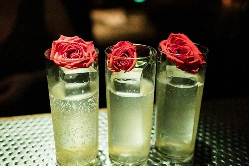Three glasses of a clear liquid with red rose decorations on a metal surface. 3