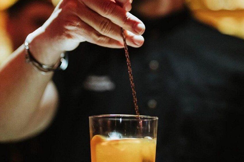 Una mano che tiene un cucchiaio sopra un bicchiere di liquido ambrato, probabilmente una bevanda. 4