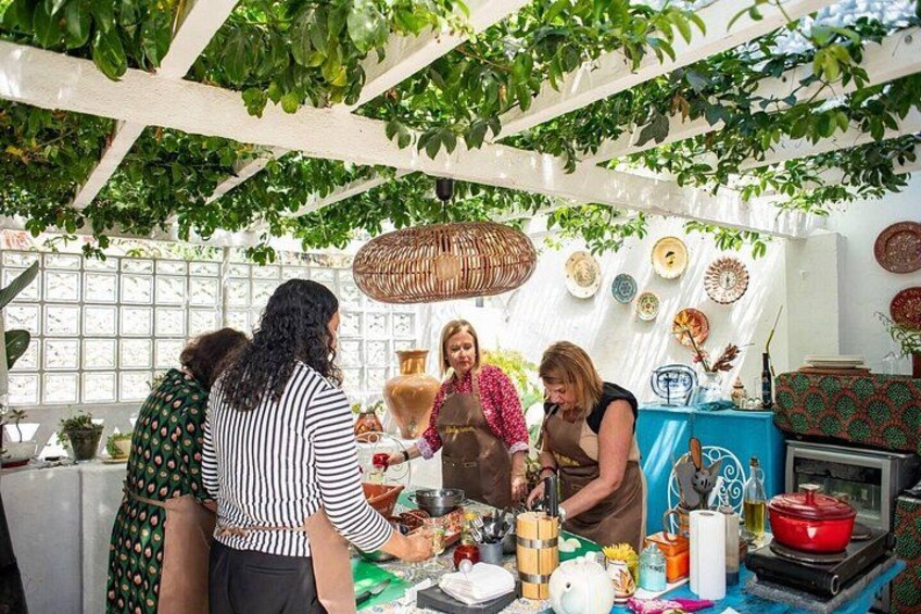A group of people in a kitchen with hanging plants, a table with food items, and decorative plates on the wall. 4