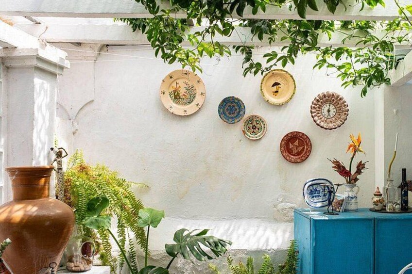 A rustic outdoor setting with a white wall adorned with various decorative plates, a blue cabinet, and a large copper pot. 3