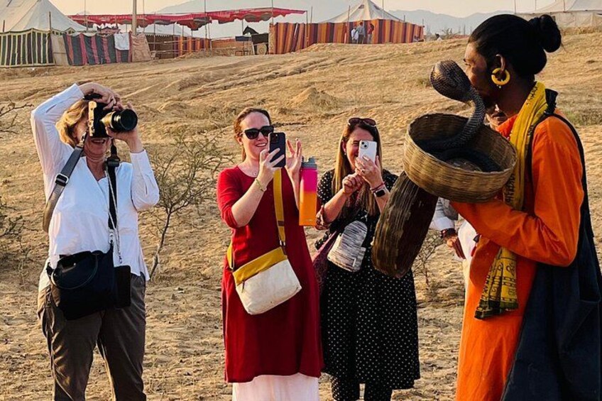 A group of people in a desert with tents and a snake in a basket. 2