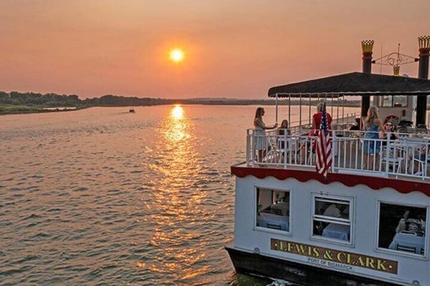 A boat with 'Lewis & Clark' written on it, docked at sunset with people on the deck. 1