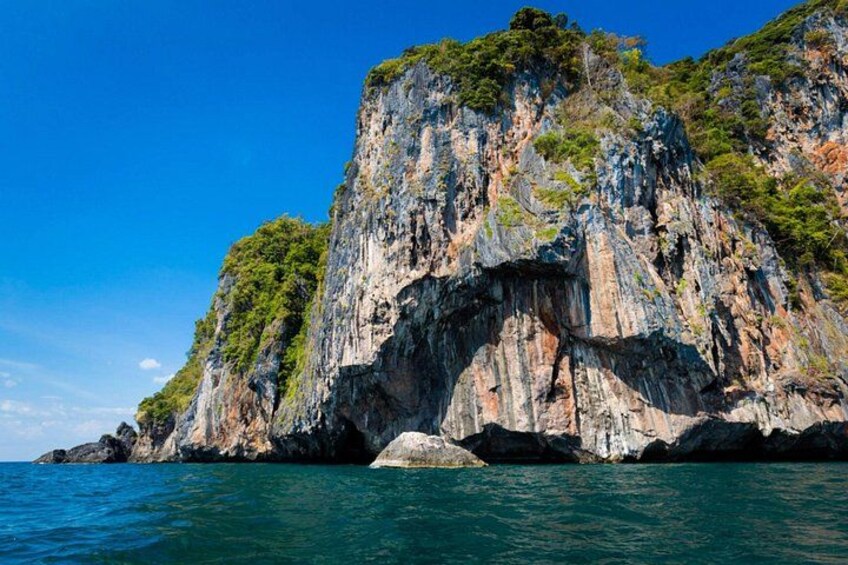 A coastal cliff with a natural arch formation, surrounded by clear blue water and lush greenery. 5