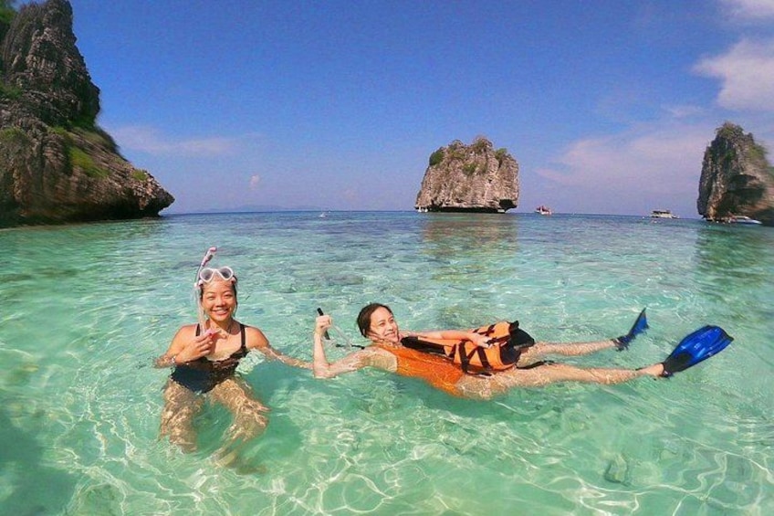 Two people snorkeling in clear turquoise water with rocky formations in the background. 1
