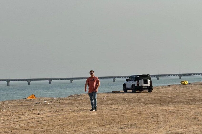 A man walking on a sandy beach with a bridge in the background. 3