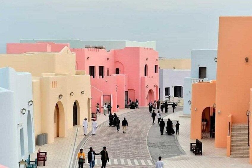 A street with buildings in pastel colors, people walking, and a clear sky. 3