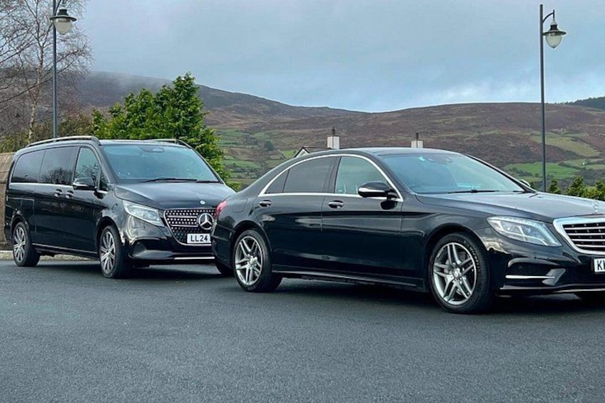 Two black Mercedes-Benz vehicles parked on a road with a hilly landscape in the background. 3