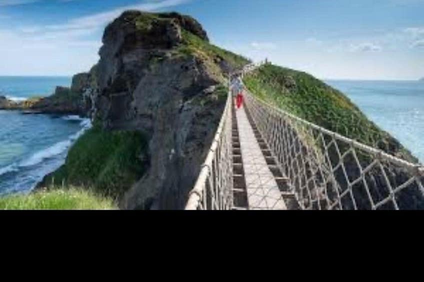 A coastal walkway with a person walking, overlooking the ocean and a rocky cliff. 5