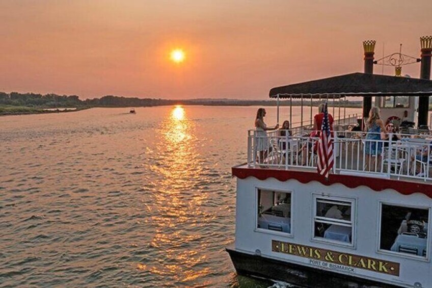 A boat with 'Lewis & Clark' written on it, docked at sunset with people on the deck. 1