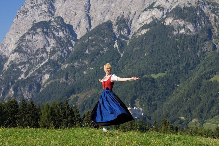 A person in traditional attire dancing in a grassy field with a mountainous backdrop. 1