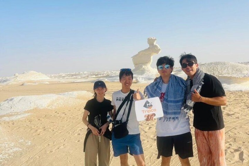 Un gruppo di persone in piedi su una spiaggia con dune di sabbia e una grande formazione rocciosa sullo sfondo. 4