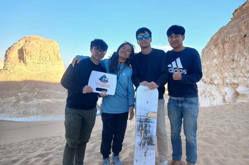 A group of people standing on a sandy beach with a large rock formation in the background. 4