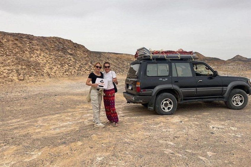 A desert landscape with a black SUV parked on the ground, a person standing next to it, and another person walking away. 3