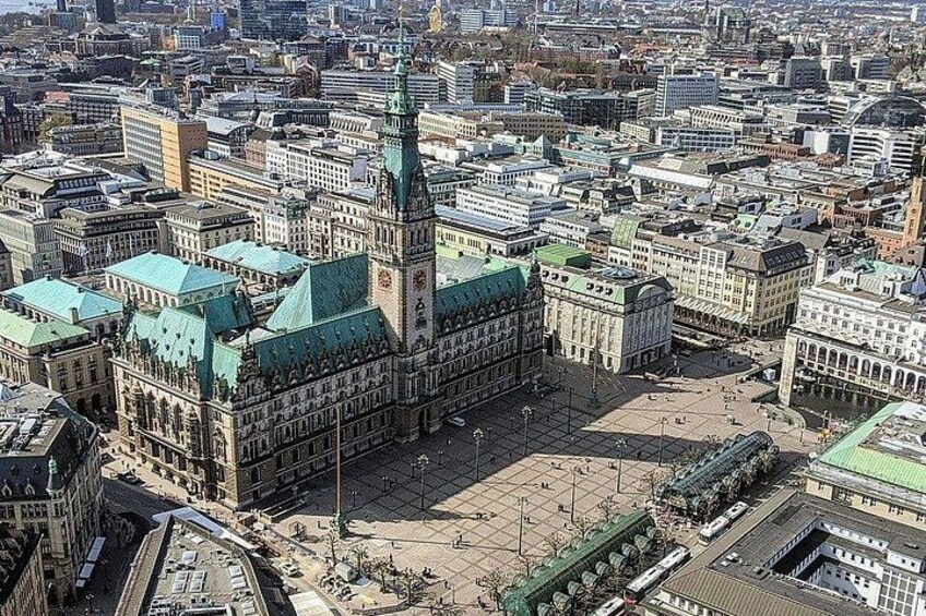 A large historic building with a prominent tower and green roofs, surrounded by a dense urban area. 5