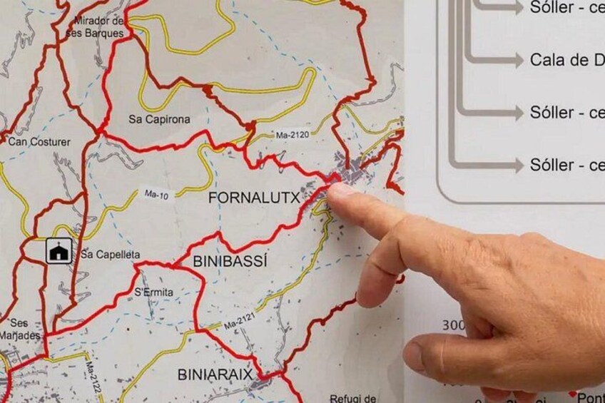 Een kaart met rode en gele lijnen die wegen aangeven, een hand die naar een locatie wijst, en plaatsnamen zoals FORNALUTX en BINIBASSI. 2