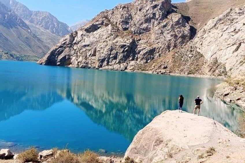 Un lac paisible, entouré de montagnes, avec deux personnes debout sur un promontoire rocheux. 1