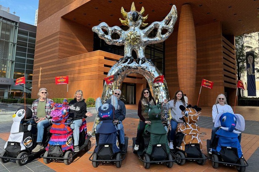 Un grupo de personas en scooters frente a un edificio con un arco decorativo grande. 2