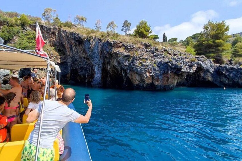A boat with people taking photos near a rocky coastline. 2