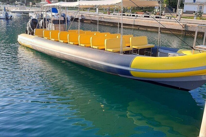 A yellow and gray inflatable boat docked at a marina with chairs and tables on board. 1