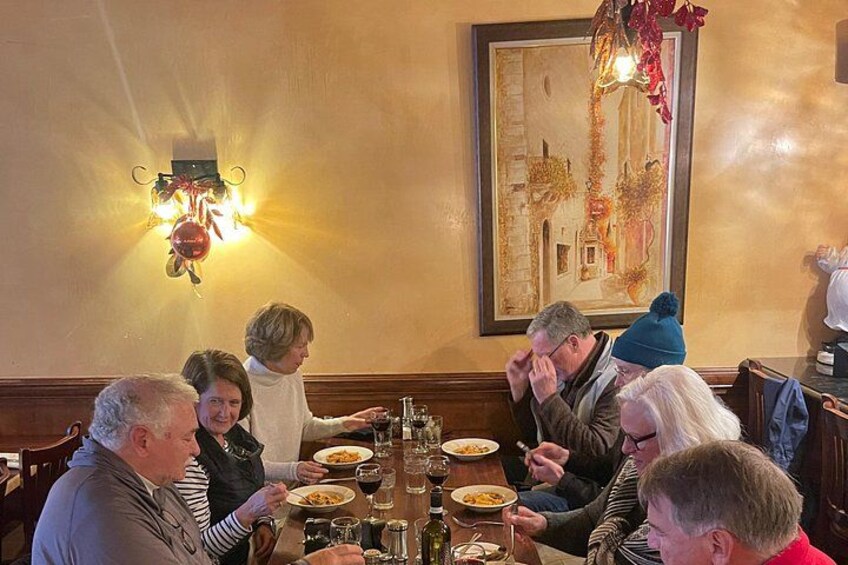 Un grupo de personas cenando en una mesa en un restaurante con luz cálida y un cuadro en la pared. 3