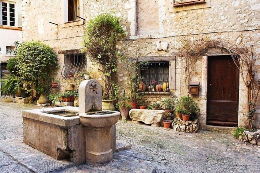 A stone well, potted plants, and a rustic building with a wooden door. 3
