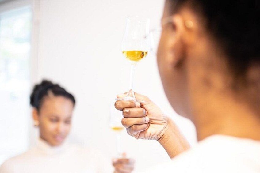 A person holding a wine glass with a yellow liquid, likely wine, in a well-lit indoor setting. 1