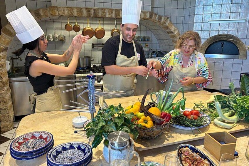 Chefs preparando alimentos en una cocina con pared de ladrillo, ollas colgantes y un horno de pizza. 2