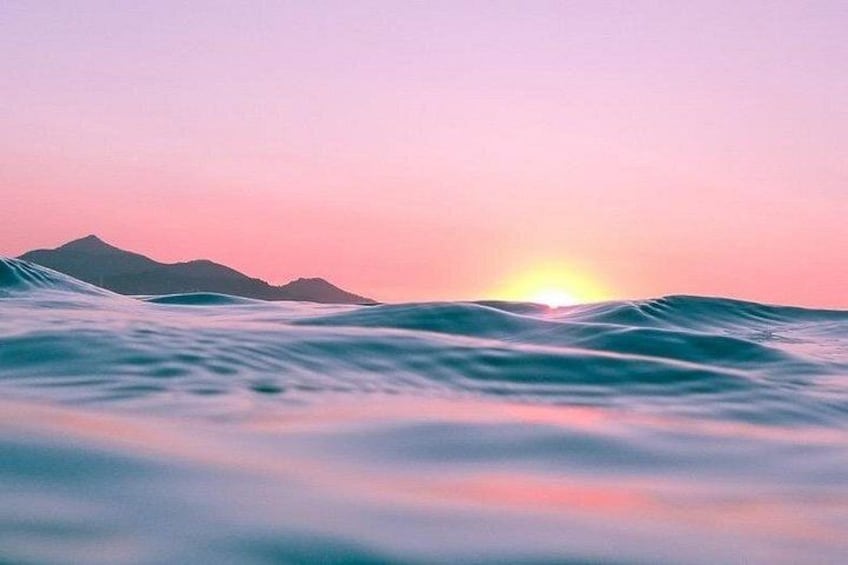 Een zonsondergang boven de oceaan met golven en een berg in de verte. 1