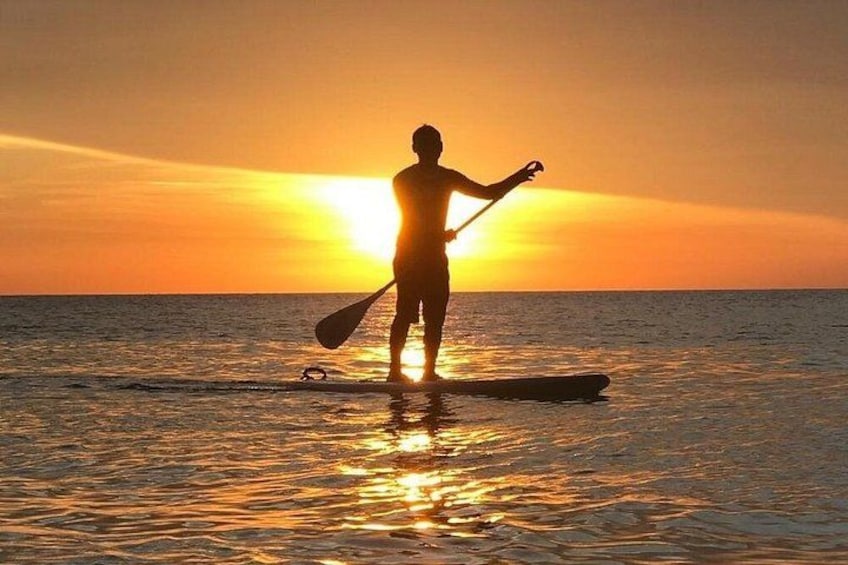 Iemand staat bij zonsondergang op een paddleboard. 3
