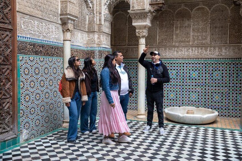 Un groupe de personnes se trouve dans une cour ornée de motifs complexes en mosaïque et dotée d’une fontaine. 2