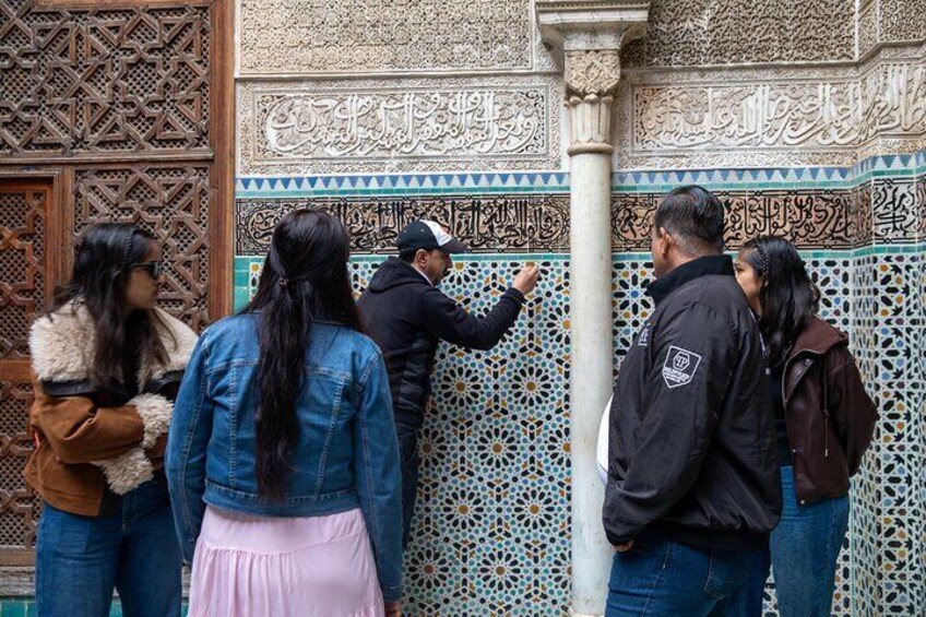 En grupp människor står och betraktar en detaljerad vägg med intrikata mönster och arabisk kalligrafi. 5