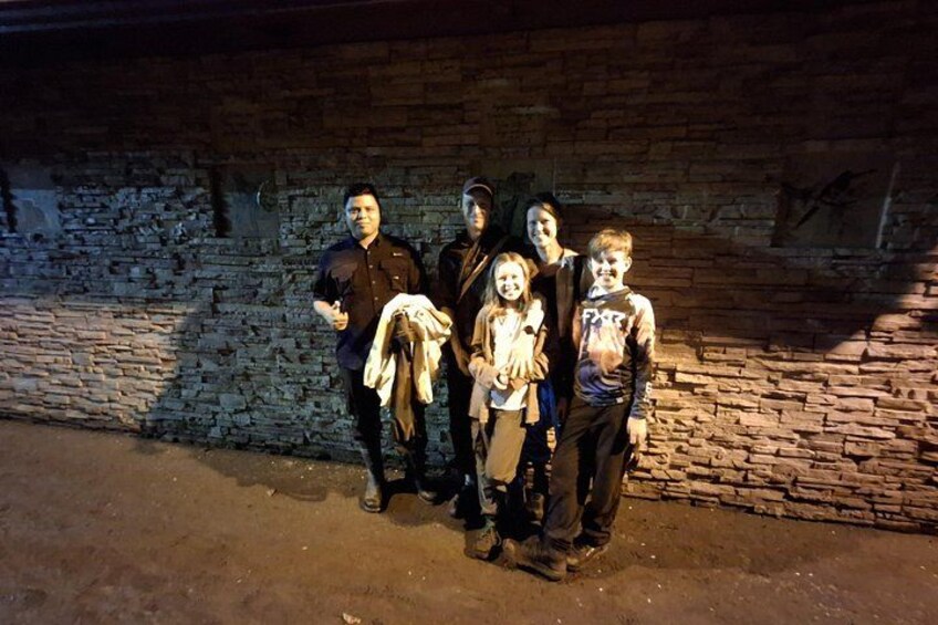 A group of people standing in front of a brick wall at night. 1