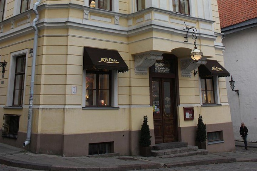 A building with a yellow facade, two awnings with the word 'Kafes' on them, a wooden door, and a street lamp. 5