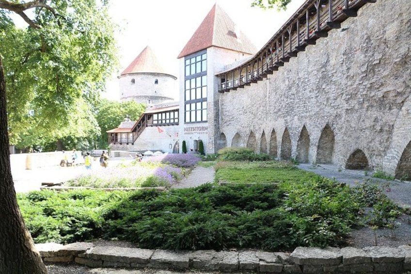 A historic stone building with a tower, a wooden walkway, and a well-maintained garden. 2