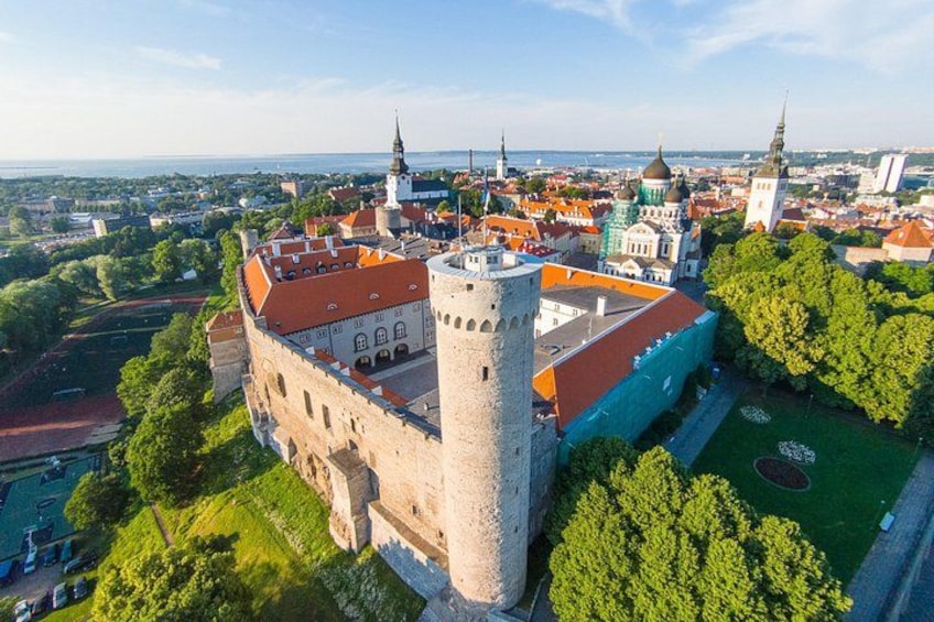 A historic castle with a prominent tower, surrounded by lush greenery and a vibrant cityscape in the background. 3