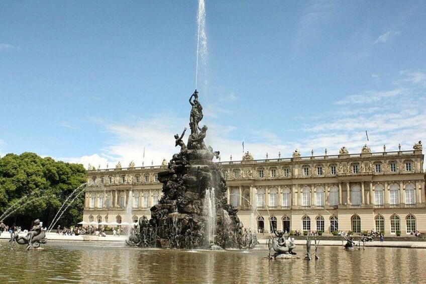 A grand fountain with statues, a large ornate building in the background, and a clear sky. 1