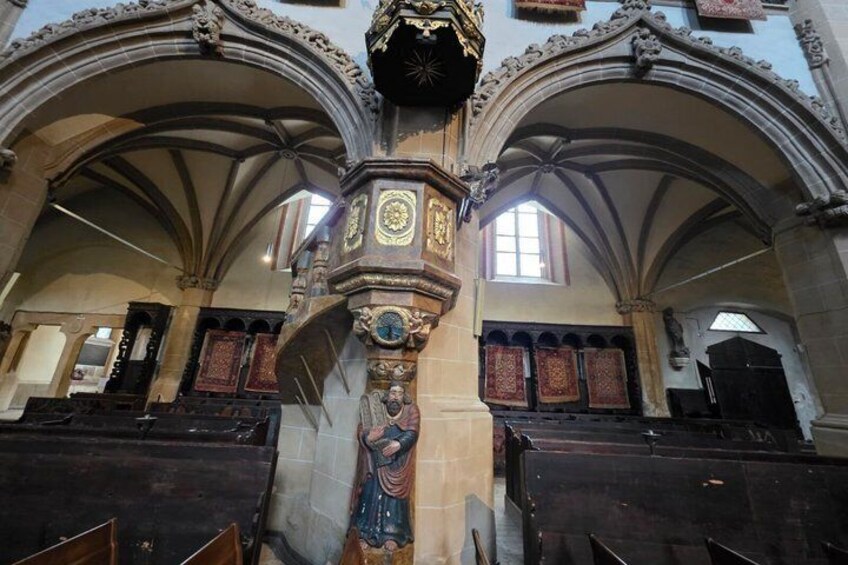 Interior de una iglesia con techos abovedados, una torre de reloj central y bancos de madera. 5