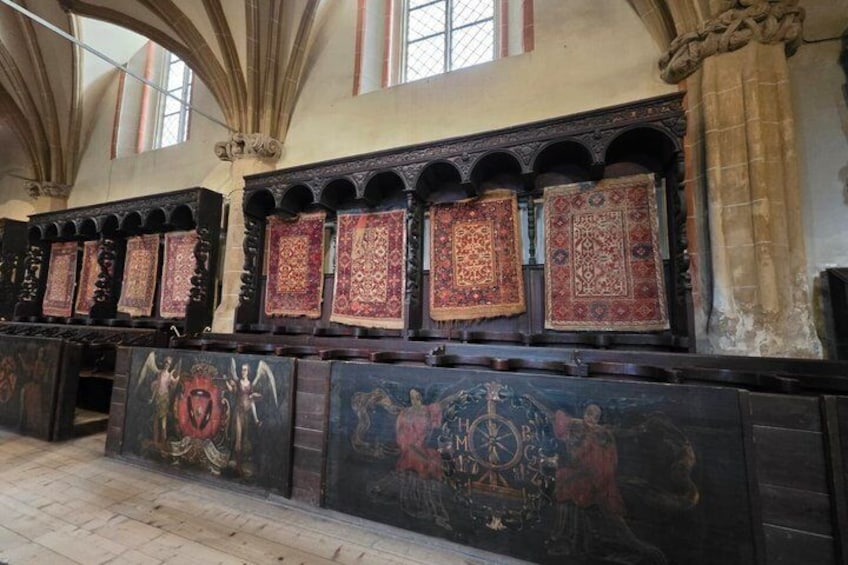 Interior de iglesia con paneles de madera ornamentados, pinturas religiosas y alfombras estampadas. 4