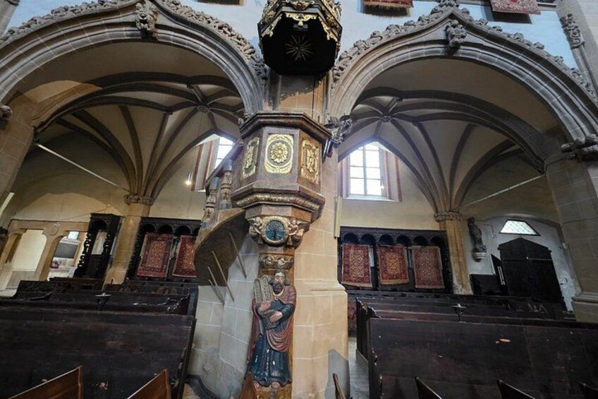 A church interior with Gothic arches, a central clock tower, and wooden pews. 3