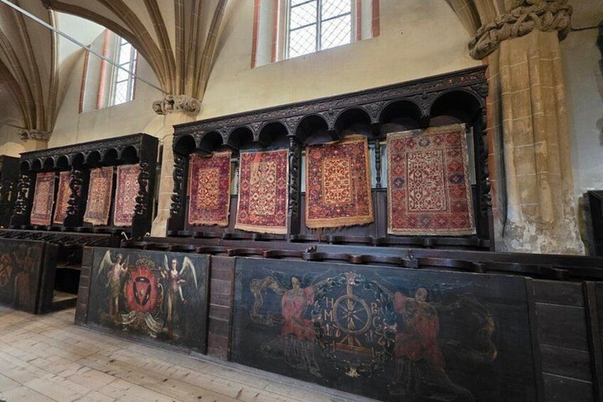 Een kerkinterieur met versierde houten panelen, religieuze schilderijen en behangtapijten met patronen. 5