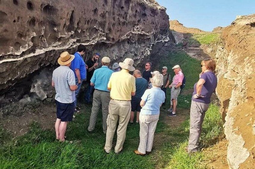 A group of people standing on a grassy slope next to a rocky cliff. 2