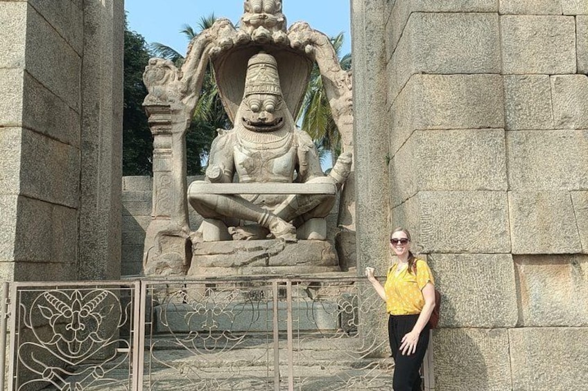 A stone statue of a deity with a large head and a seated posture, surrounded by stone pillars and a metal gate with a floral design. 4