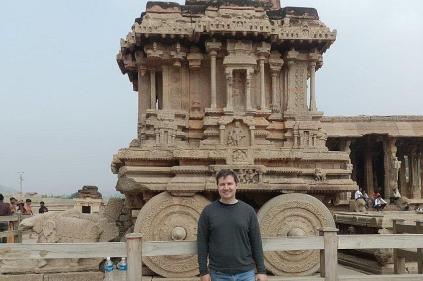 A man standing in front of a large, intricately carved stone structure with multiple tiers and detailed carvings. 2