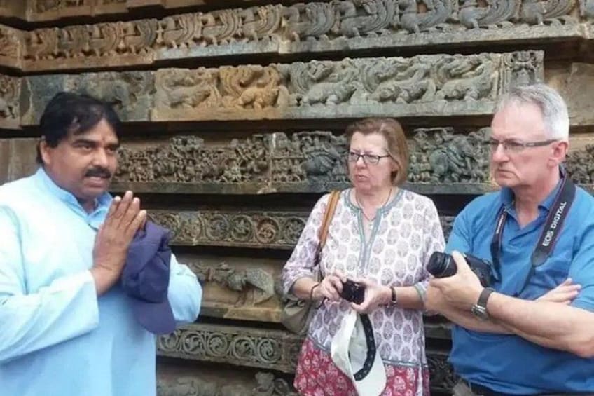 Three people standing in front of a stone wall with intricate carvings. 1