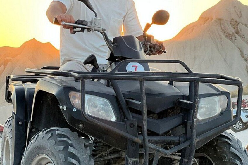 A person riding a black ATV with a number 7 on the front, in a desert landscape with mountains in the background. 2