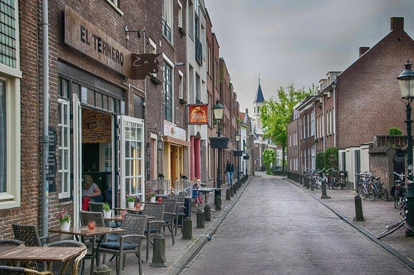 Een straat met kinderkopjes, omringd door bakstenen gebouwen, met terrasjes en fietsen langs de stoep. 3