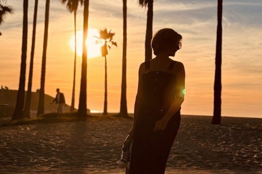 Una persona de pie en la playa con palmeras y el sol poniéndose al fondo. 2