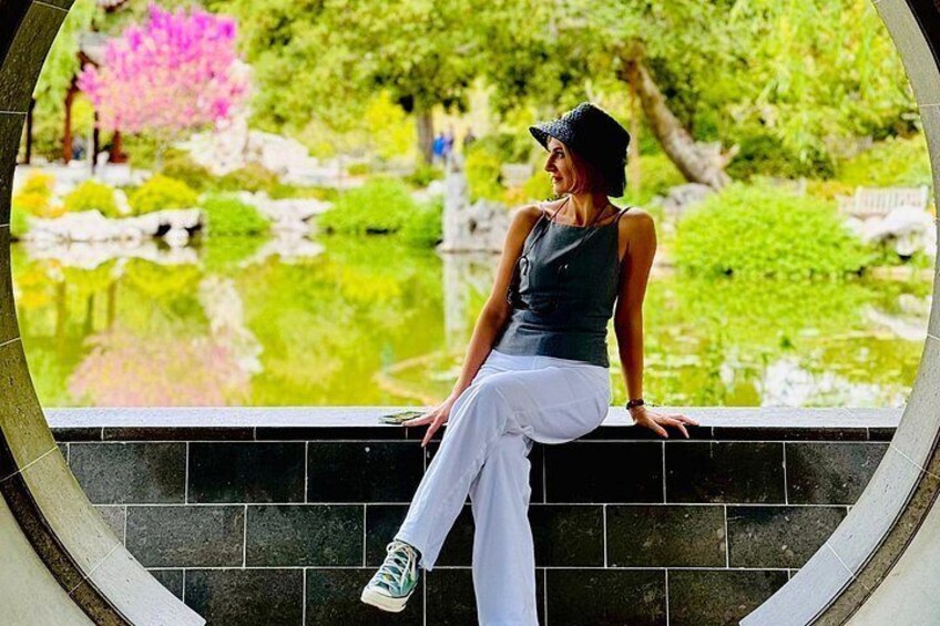 Una persona sentada en un borde de baldosas con vista a un jardín con un estanque y árboles. 4