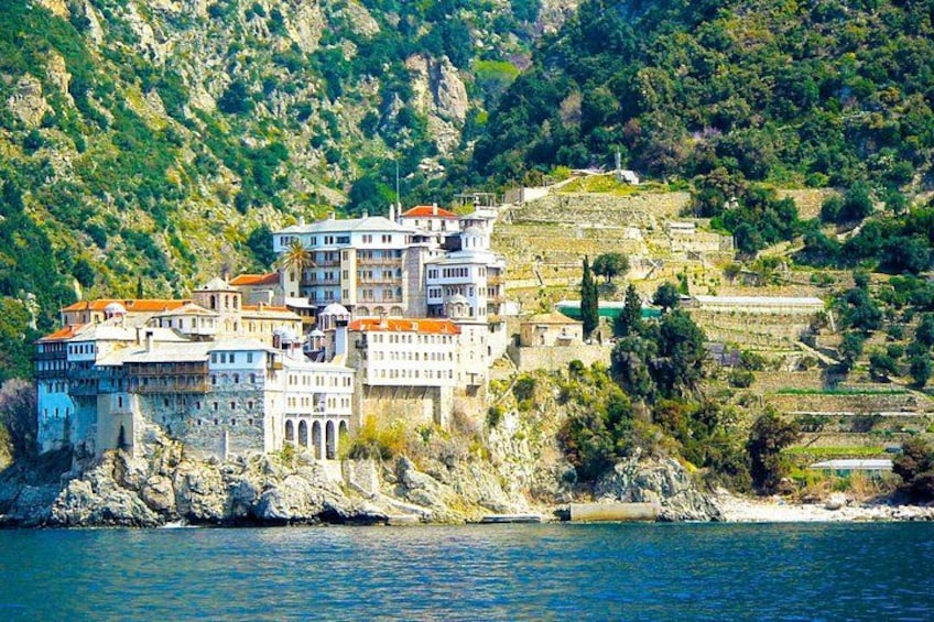 A coastal town with buildings on a hillside, a body of water in the foreground, and a mountainous backdrop. 3