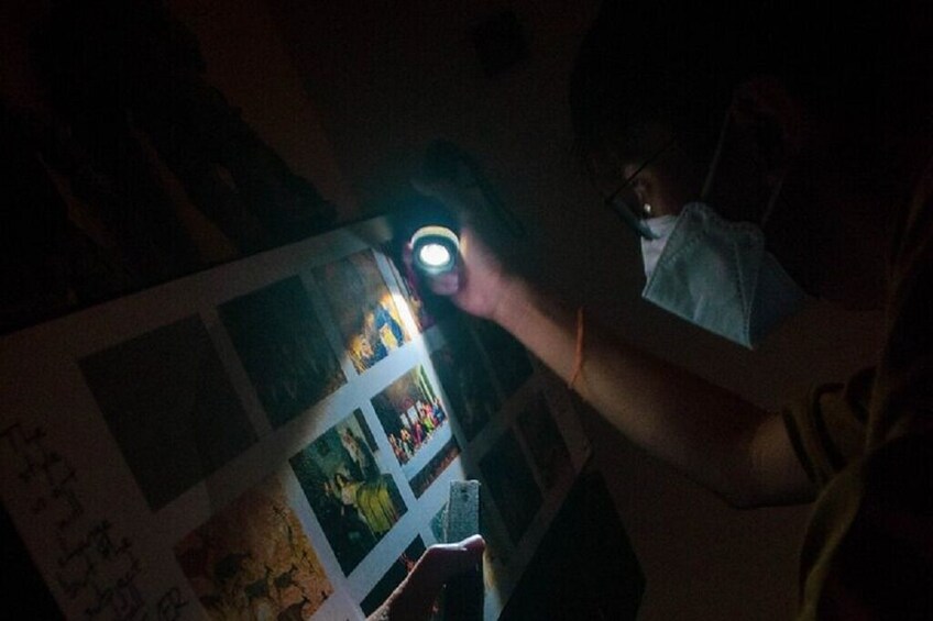 Iemand houdt een zaklamp vast, die een foto aan de muur verlicht. 5